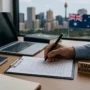 Australian small business owner reviewing legal compliance checklist with laptop and documents on desk, city skyline and Australian flag visible through window, natural daylight, realistic photo.